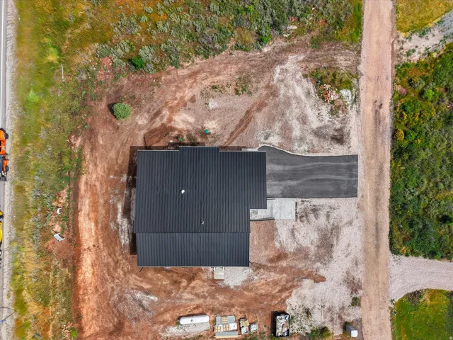 New construction with a dark metal roof, featuring a paved driveway and an adjacent gravel road