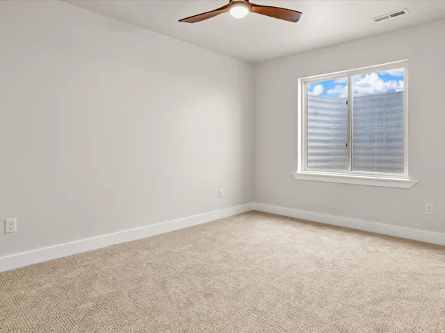 Neutral-toned room featuring a window with a white frame and sill, beige carpet flooring, and a ceiling fan with wood-finish blades