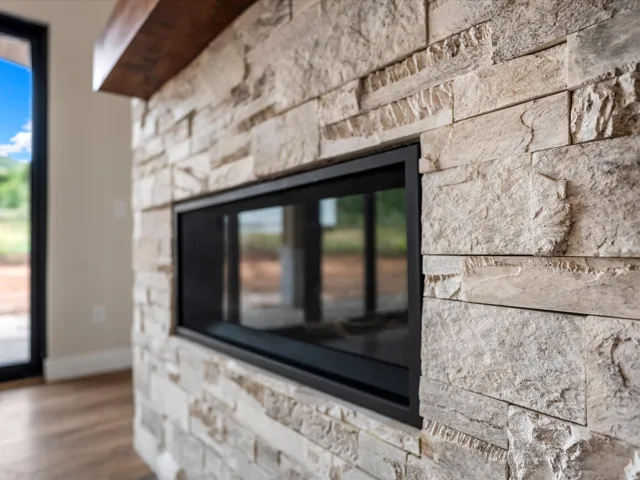 Modern linear fireplace with a black frame, surrounded by stacked stone detailing, and topped with a substantial wood mantel