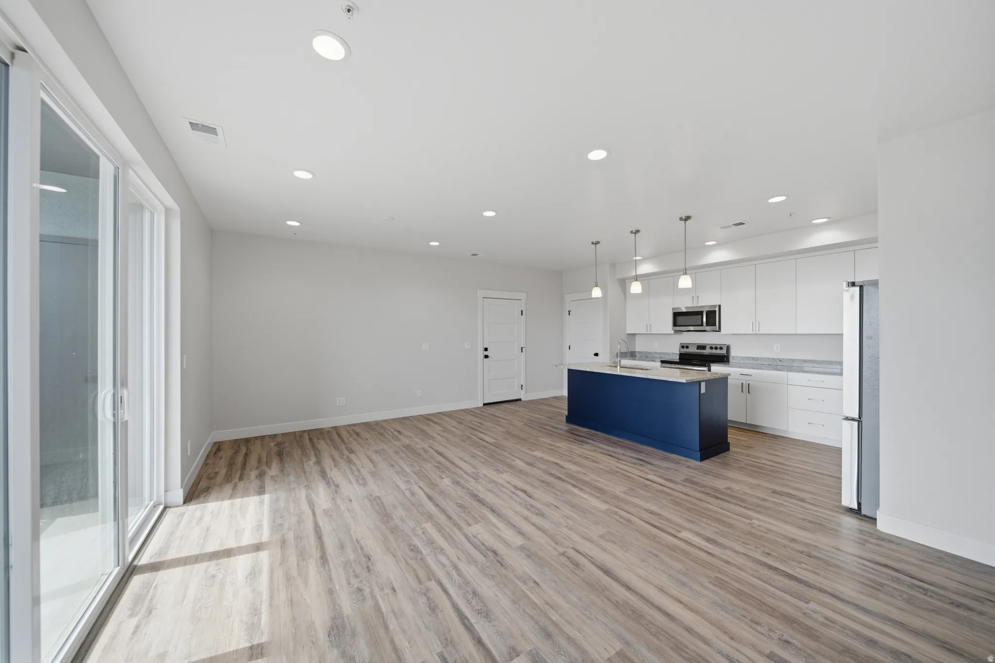 Open-concept living space featuring wood-finish flooring, recessed lighting, and a sliding glass door