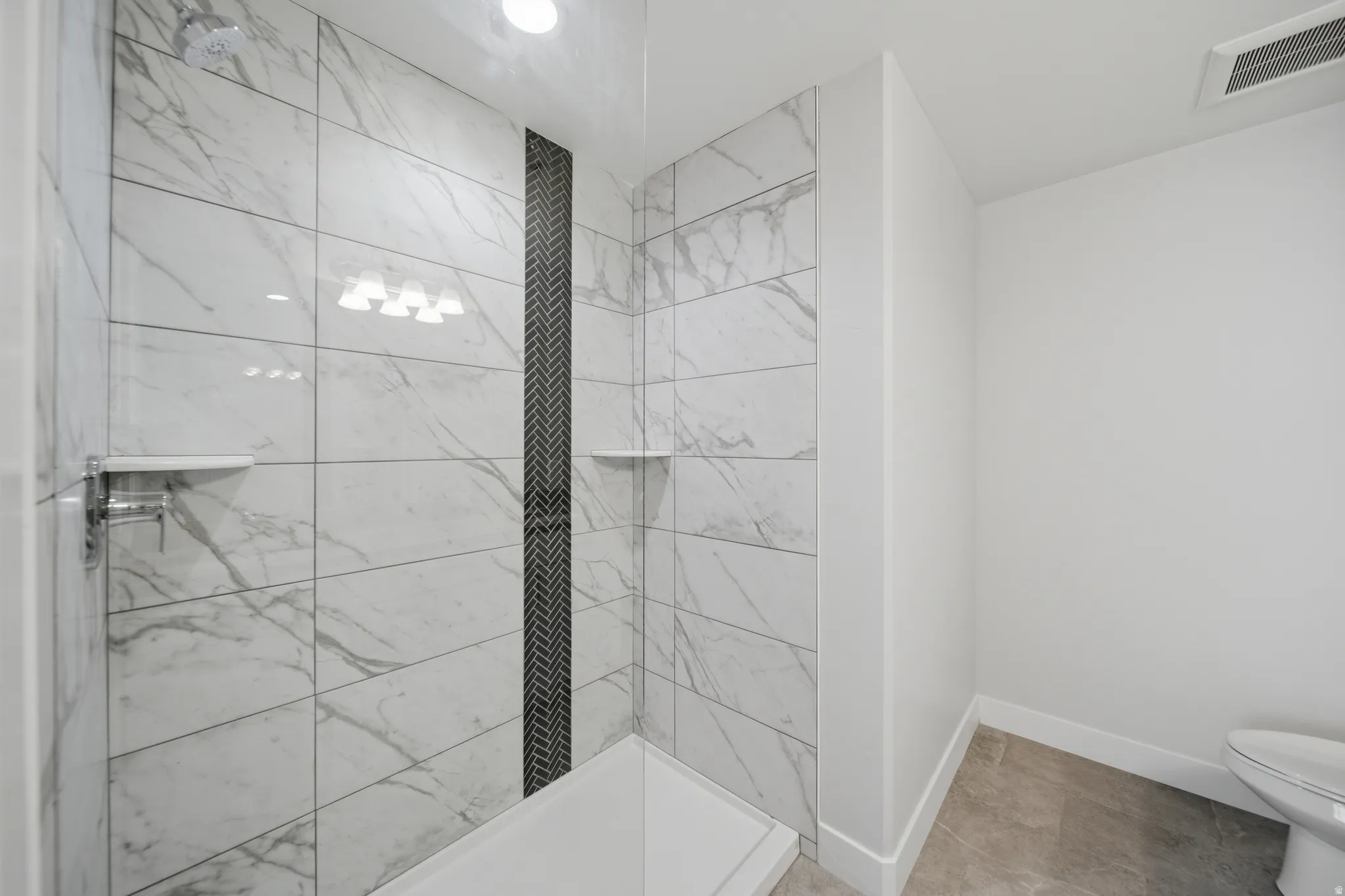 Shower enclosure with large format white and grey veined tiles, a dark grey herringbone accent column, and integrated shelving