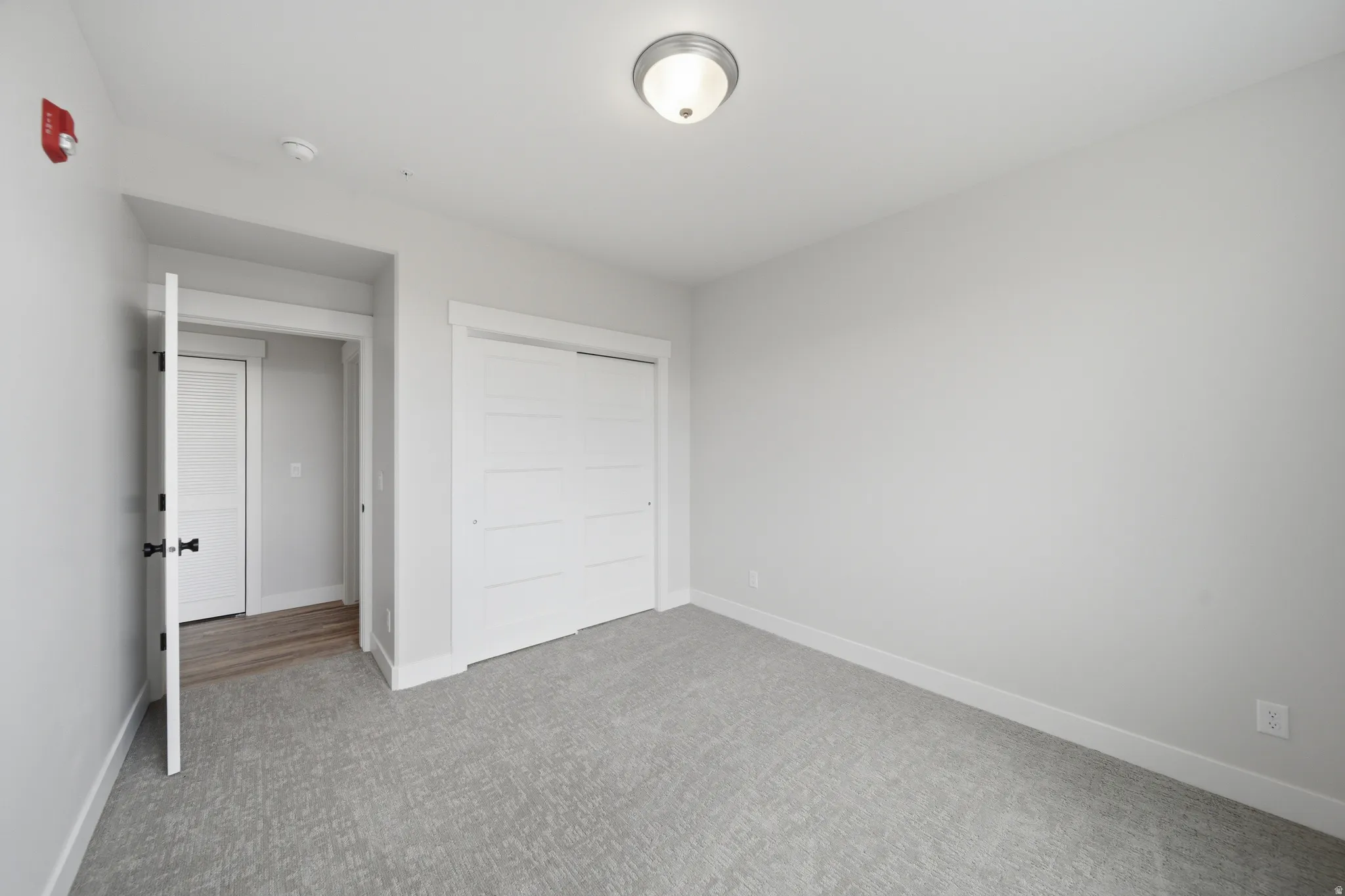 Spacious room featuring light gray walls, textured gray carpet, and white baseboards