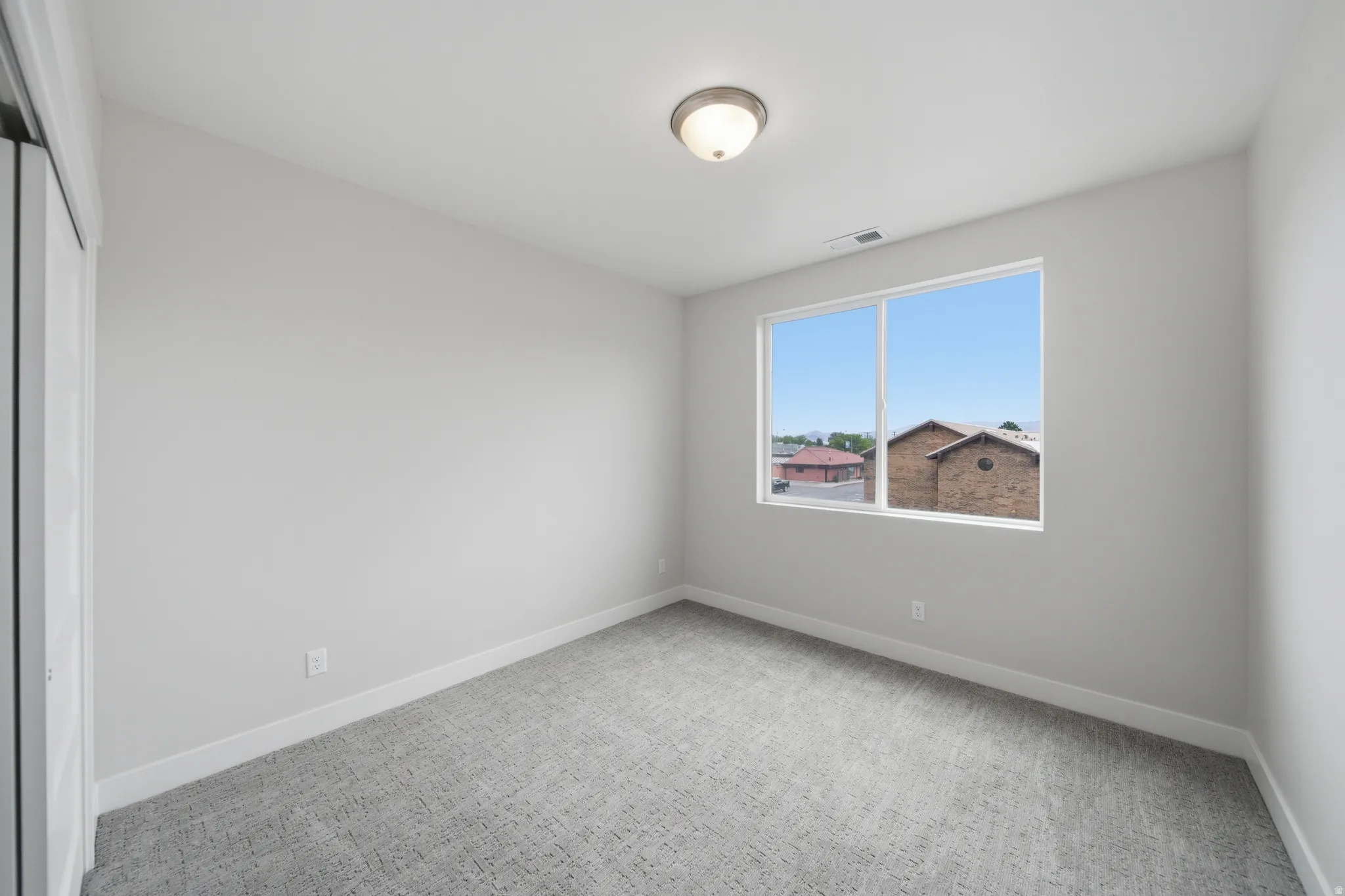 Bright room featuring a large window, textured gray carpeting, white baseboards, and a flush-mount ceiling light
