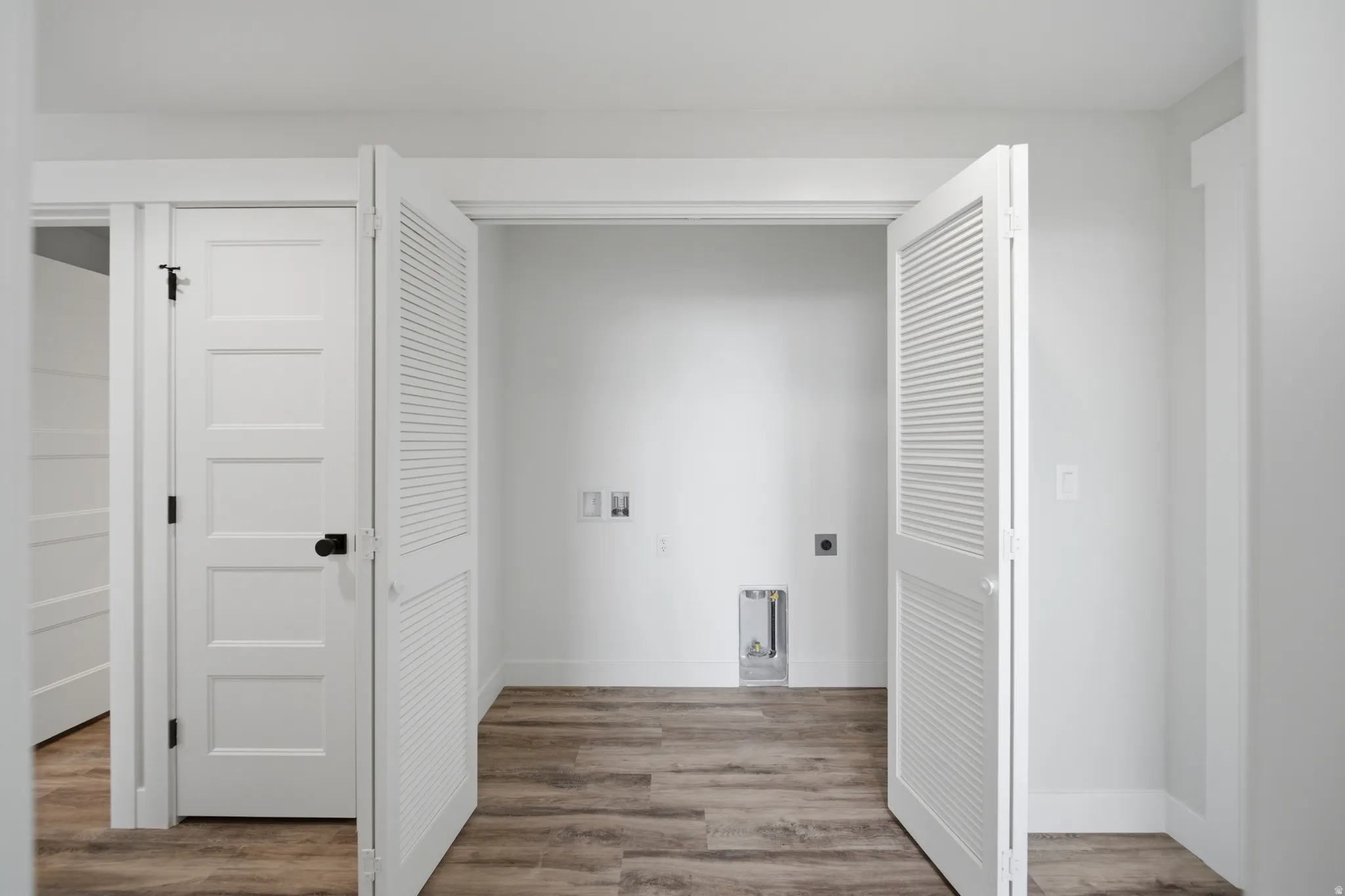 Laundry area featuring wood-finish flooring, white walls, and bi-fold louvered doors