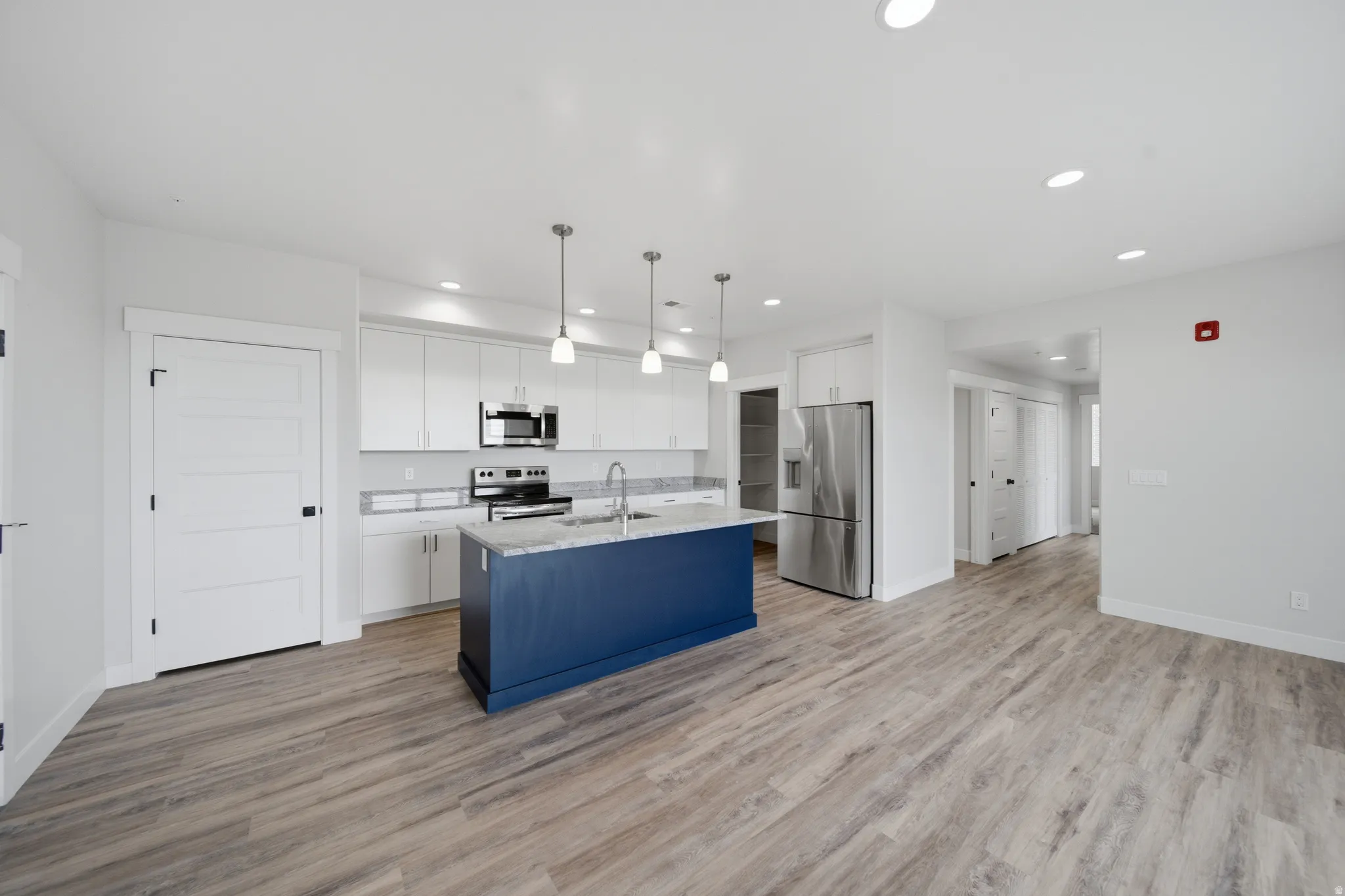 Open-concept kitchen and living area featuring wood-finish flooring, white cabinetry, stainless steel appliances, and a central island with a blue base and light-toned countertop