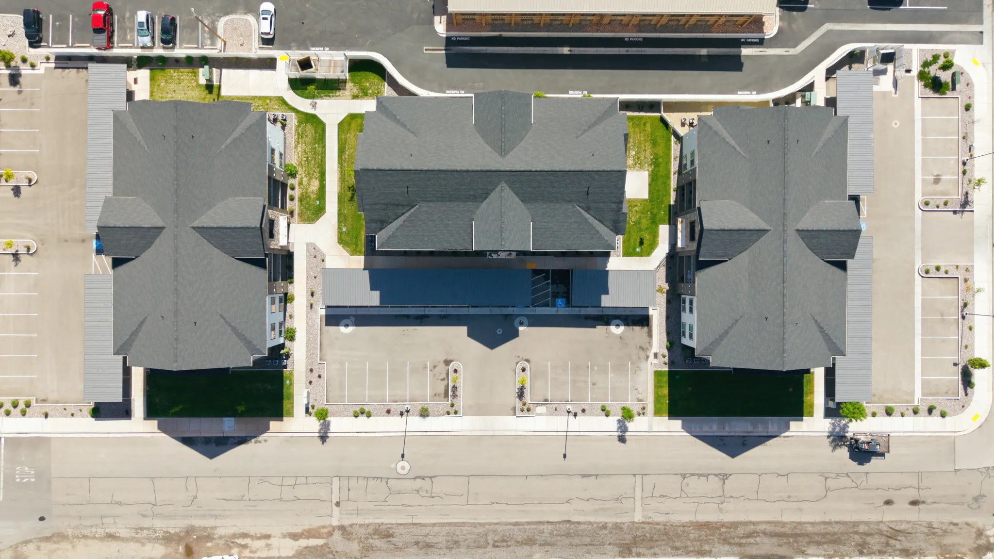 Aerial perspective of a multi-building property featuring ample surface parking, manicured green spaces, and contemporary architectural design