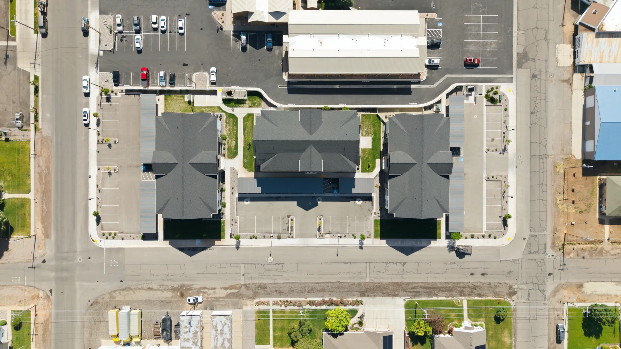 Central building complex featuring three structures with dark shingled roofs and extensive paved parking areas