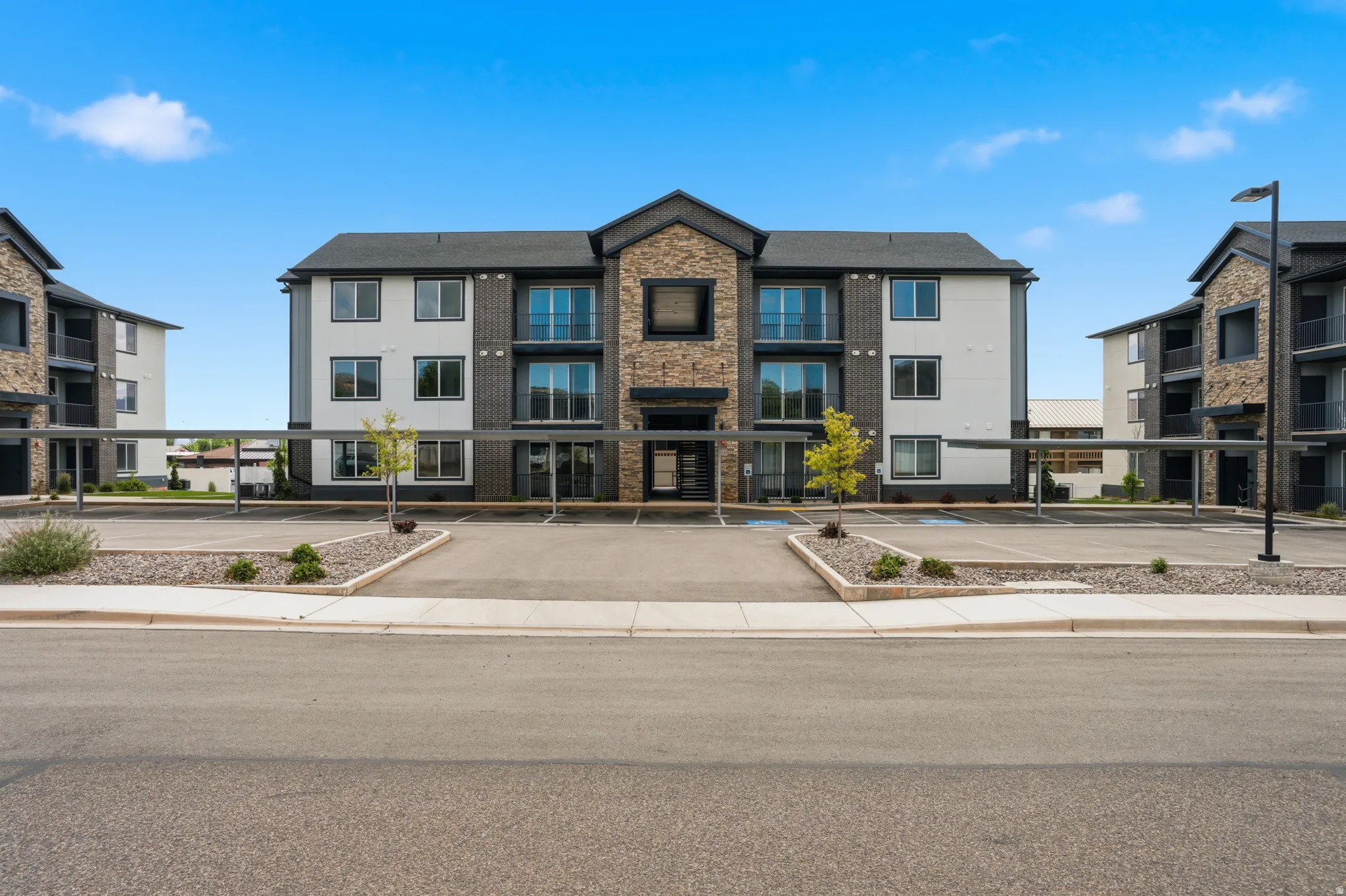 Modern apartment building featuring a stone and siding exterior, private balconies, covered parking, and an expansive asphalt parking lot