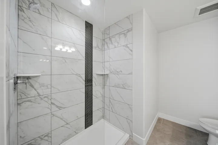 Shower enclosure with large format white and grey veined tiles, a dark grey herringbone accent column, and integrated shelving