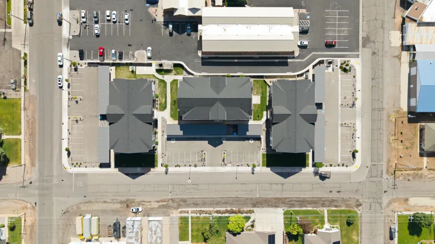 Central building complex featuring three structures with dark shingled roofs and extensive paved parking areas