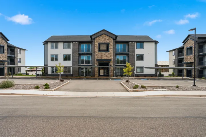 Modern apartment building featuring a stone and siding exterior, private balconies, covered parking, and an expansive asphalt parking lot