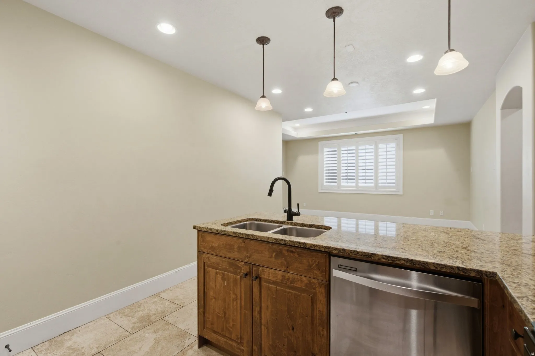 Kitchen island featuring a dual-basin stainless steel sink with a matte black gooseneck faucet, light-toned stone countertop, and integrated stainless steel dishwasher