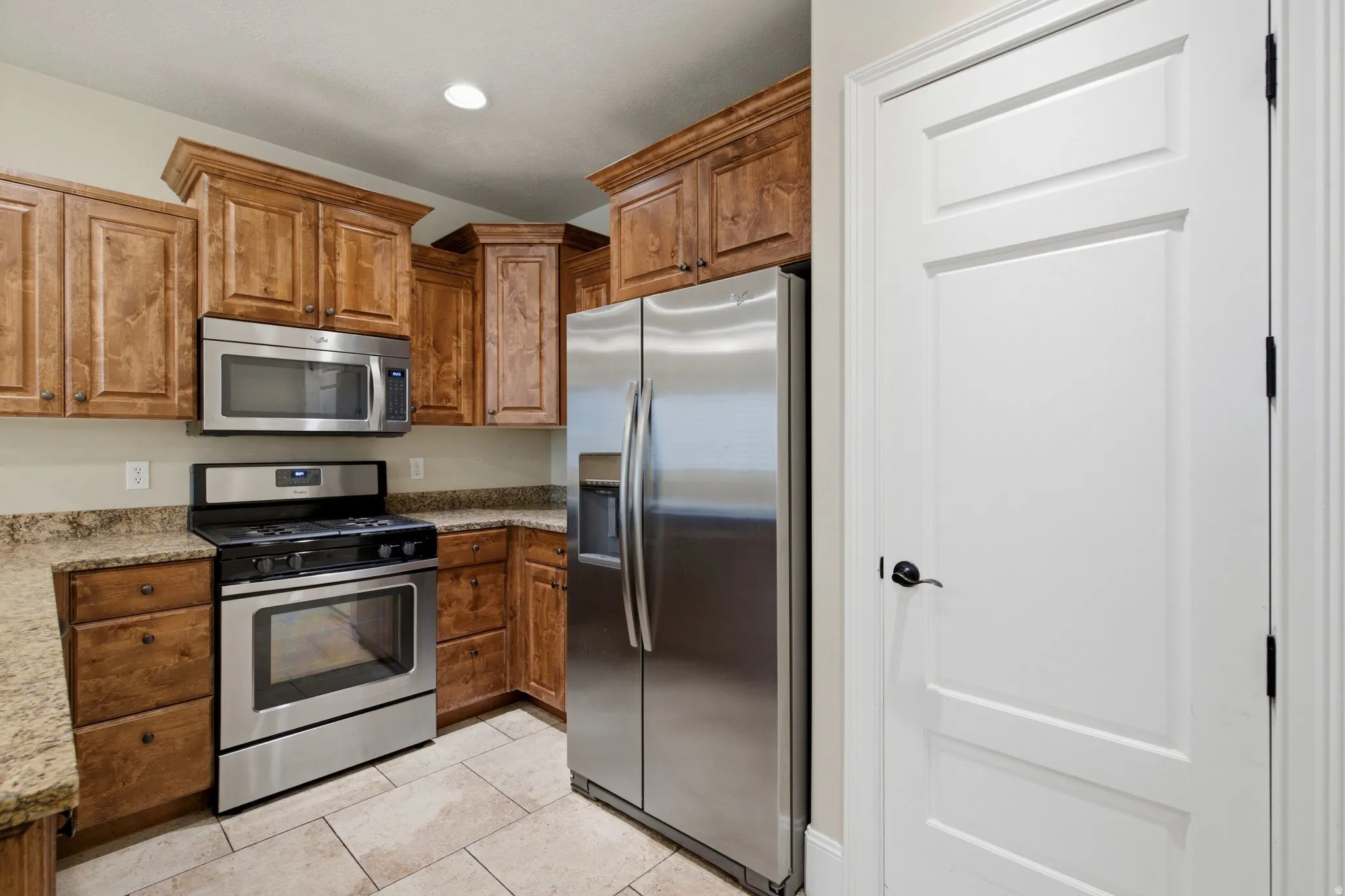 Kitchen featuring wood cabinetry, stainless steel appliances, speckled countertops, and neutral-toned tile flooring