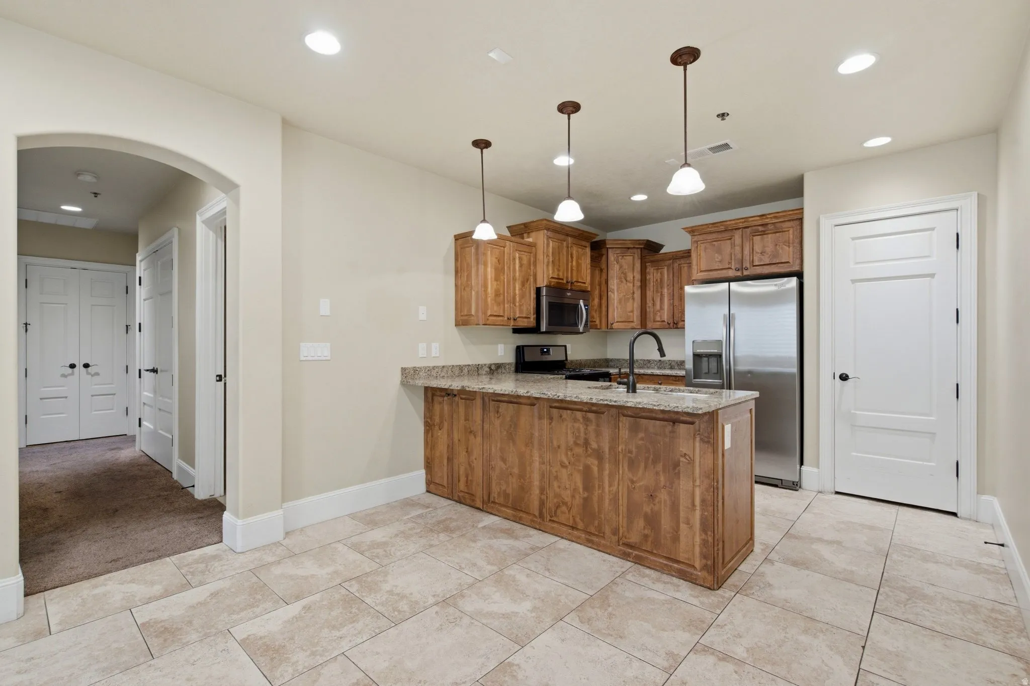 Kitchen featuring a central island with a sink, wood-finish cabinetry, light-toned stone countertops, and stainless steel appliances