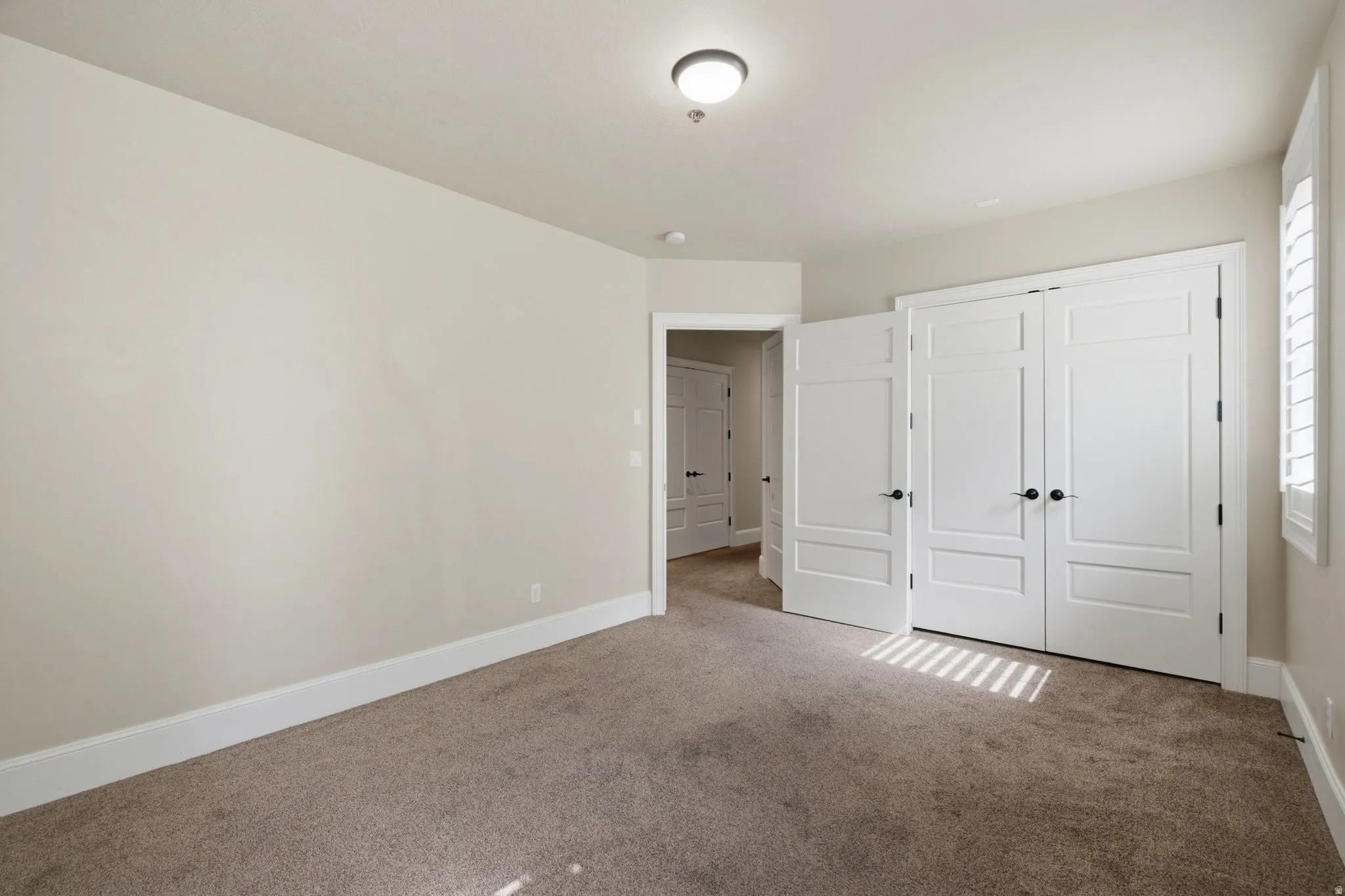 Carpeted room featuring white trim, white paneled doors with black hardware, and a window with white louvered shutters