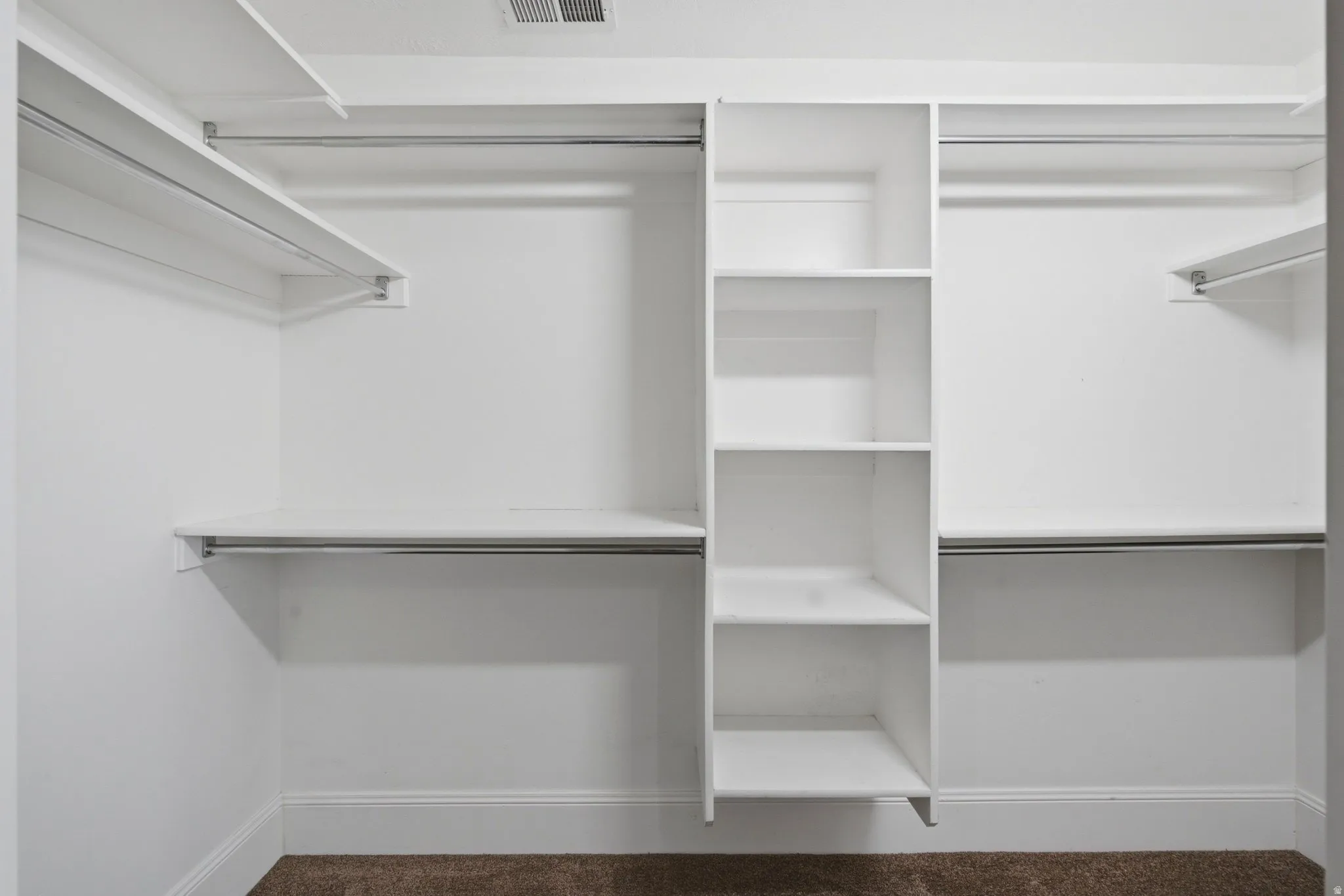 Walk-in closet featuring built-in shelving, multiple hanging rods, white-painted walls, and brown carpet flooring