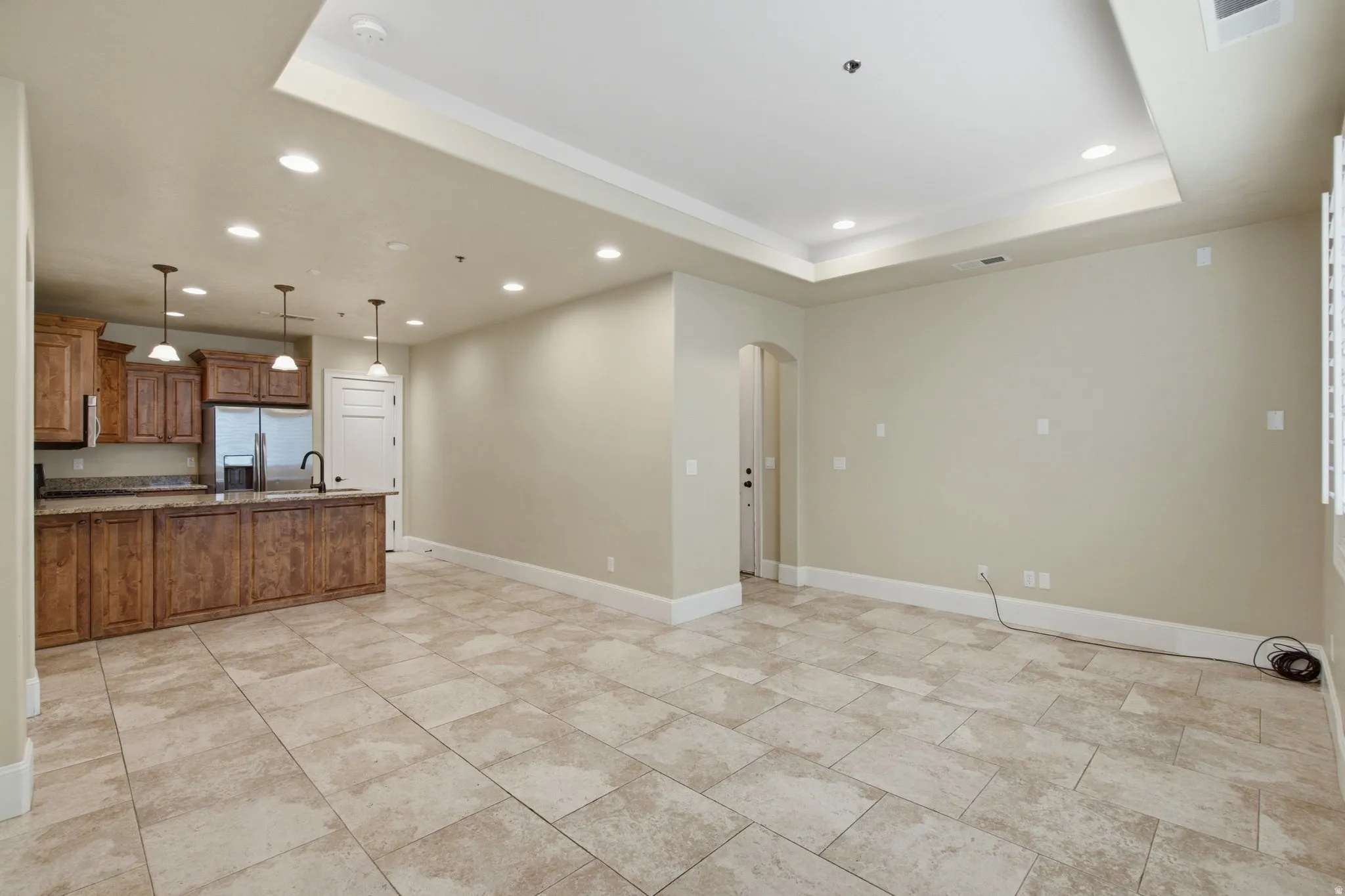 Open-concept living area featuring large format tile flooring, a tray ceiling with recessed lighting, and a kitchen island with pendant lighting
