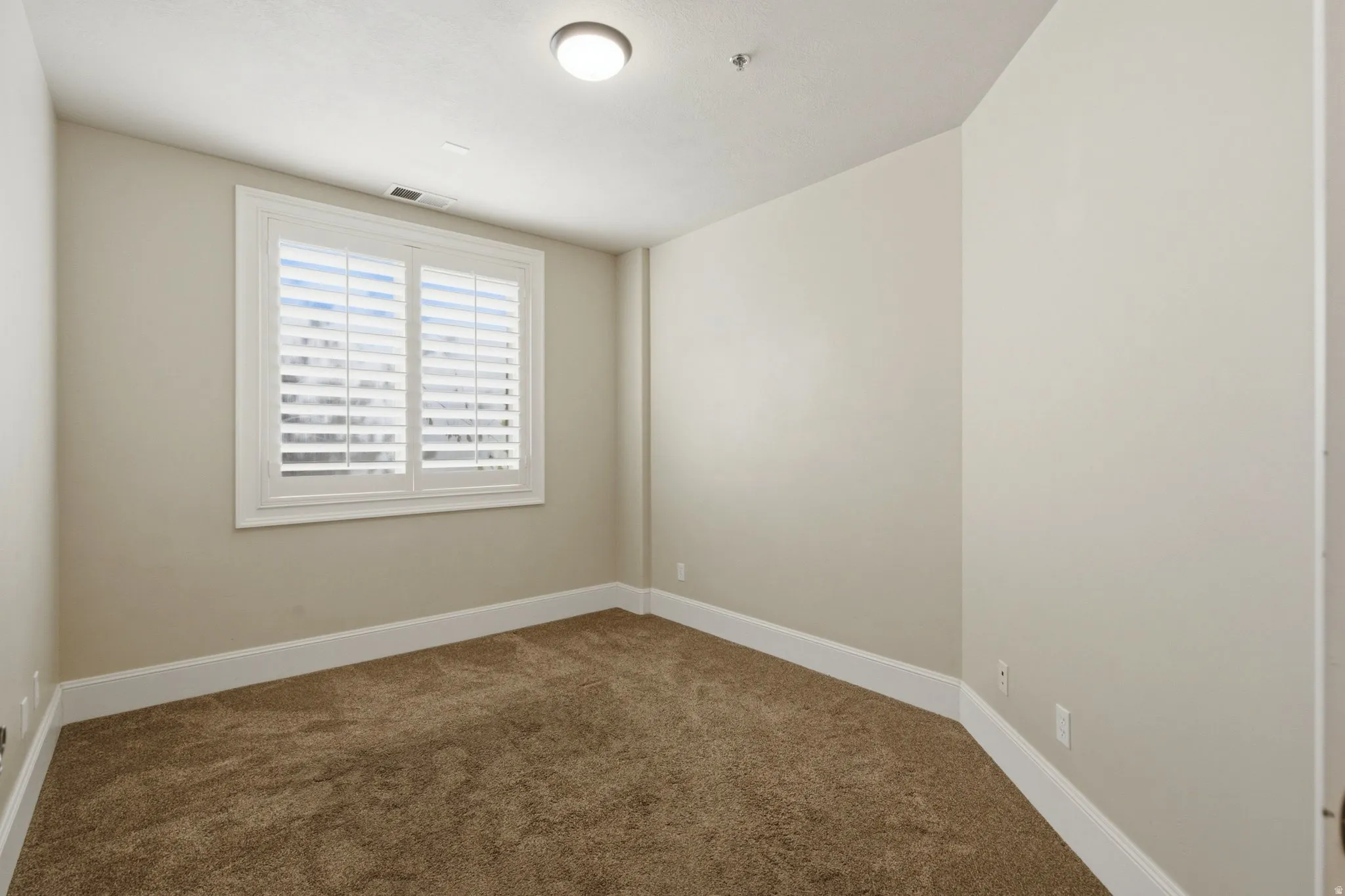 Carpeted room featuring a window with white plantation shutters, neutral wall paint, white baseboards, and a flush-mount ceiling light fixture