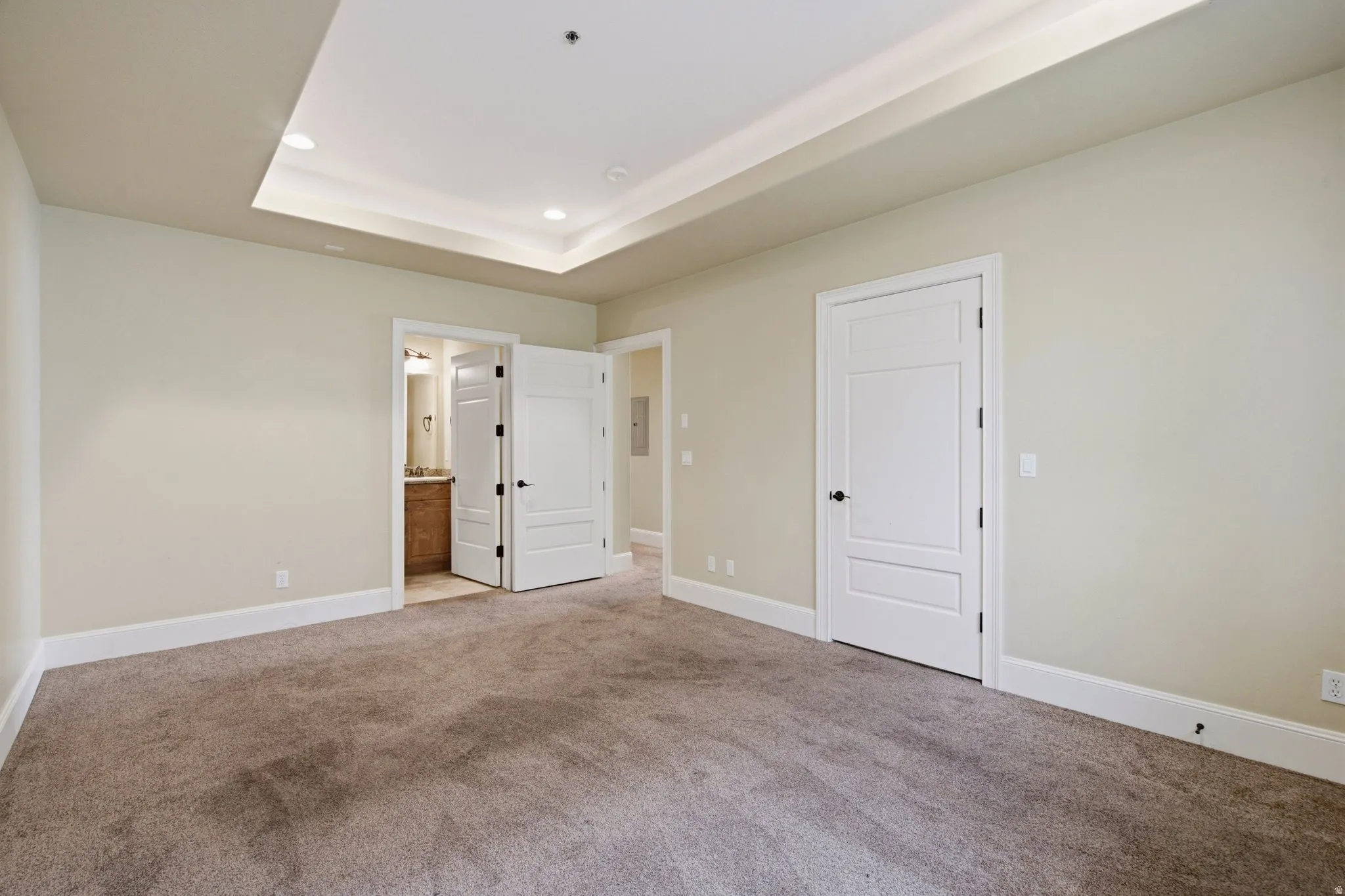 Carpeted room featuring a tray ceiling with recessed lighting, crown molding, and two panel doors