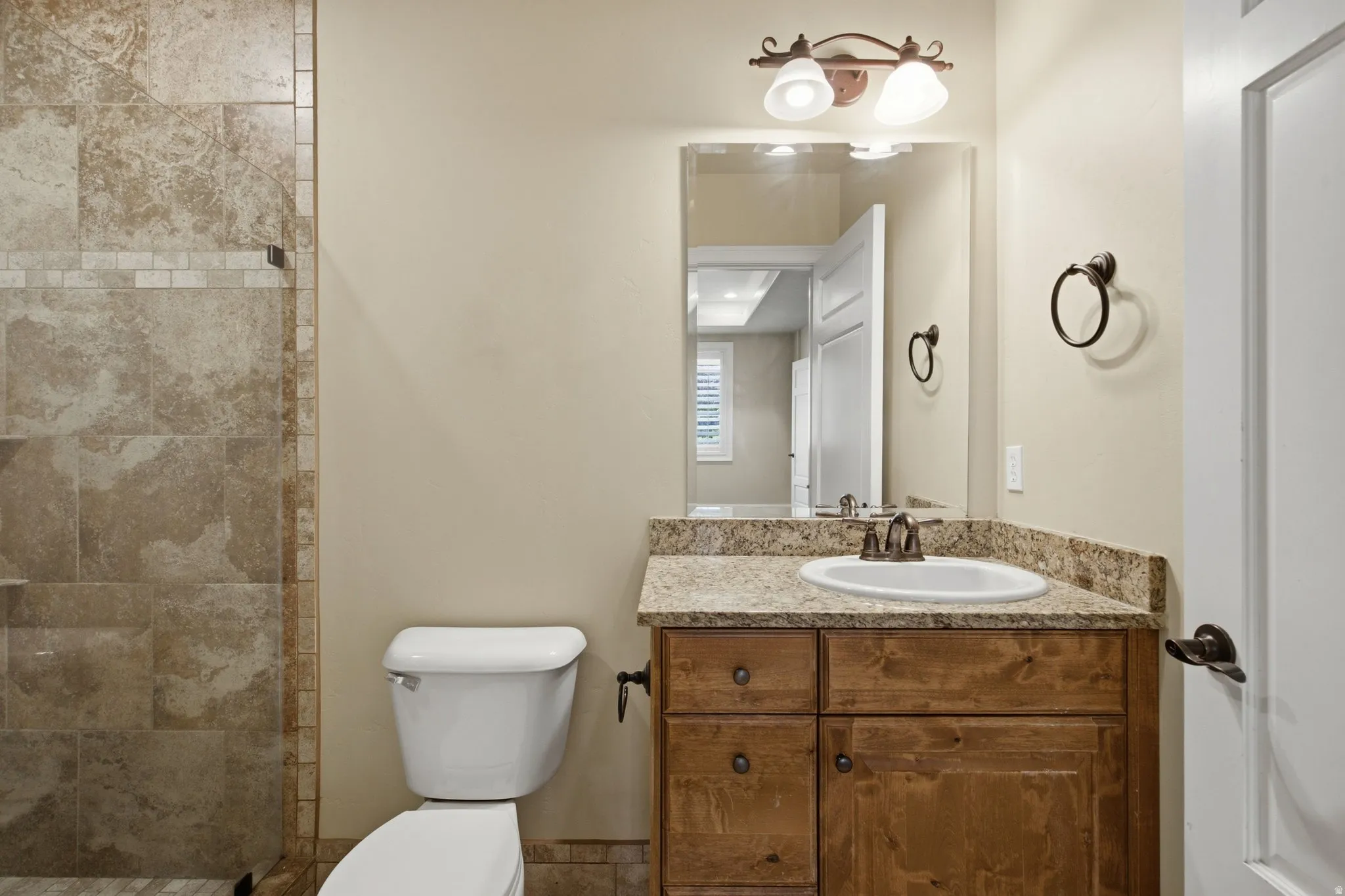 Bathroom featuring a wood-finish vanity with an undermount sink, a stone-finish countertop, and a tiled shower with a glass enclosure