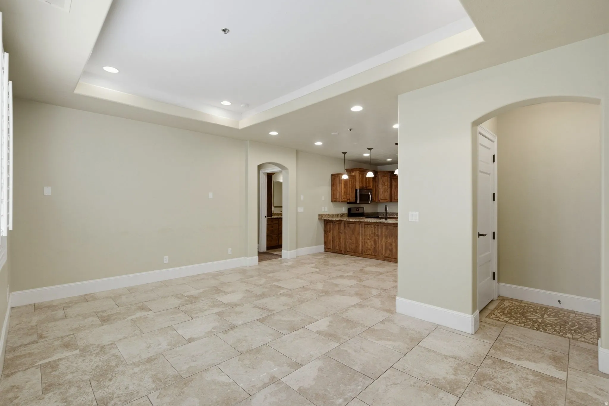 Spacious living area featuring large format tile flooring, a tray ceiling with recessed lighting, and white baseboards