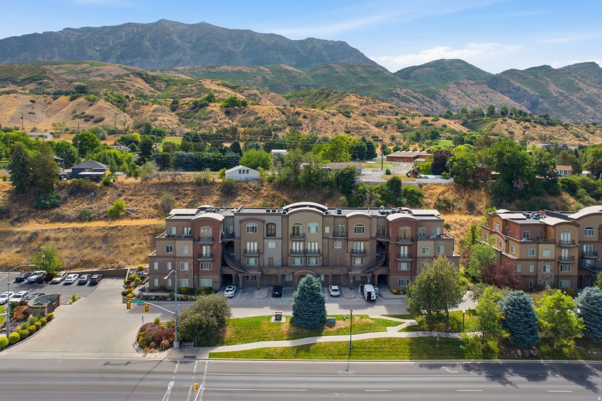 Multi-story residential building featuring brick and stucco exterior finishes, individual balconies, and a paved parking area