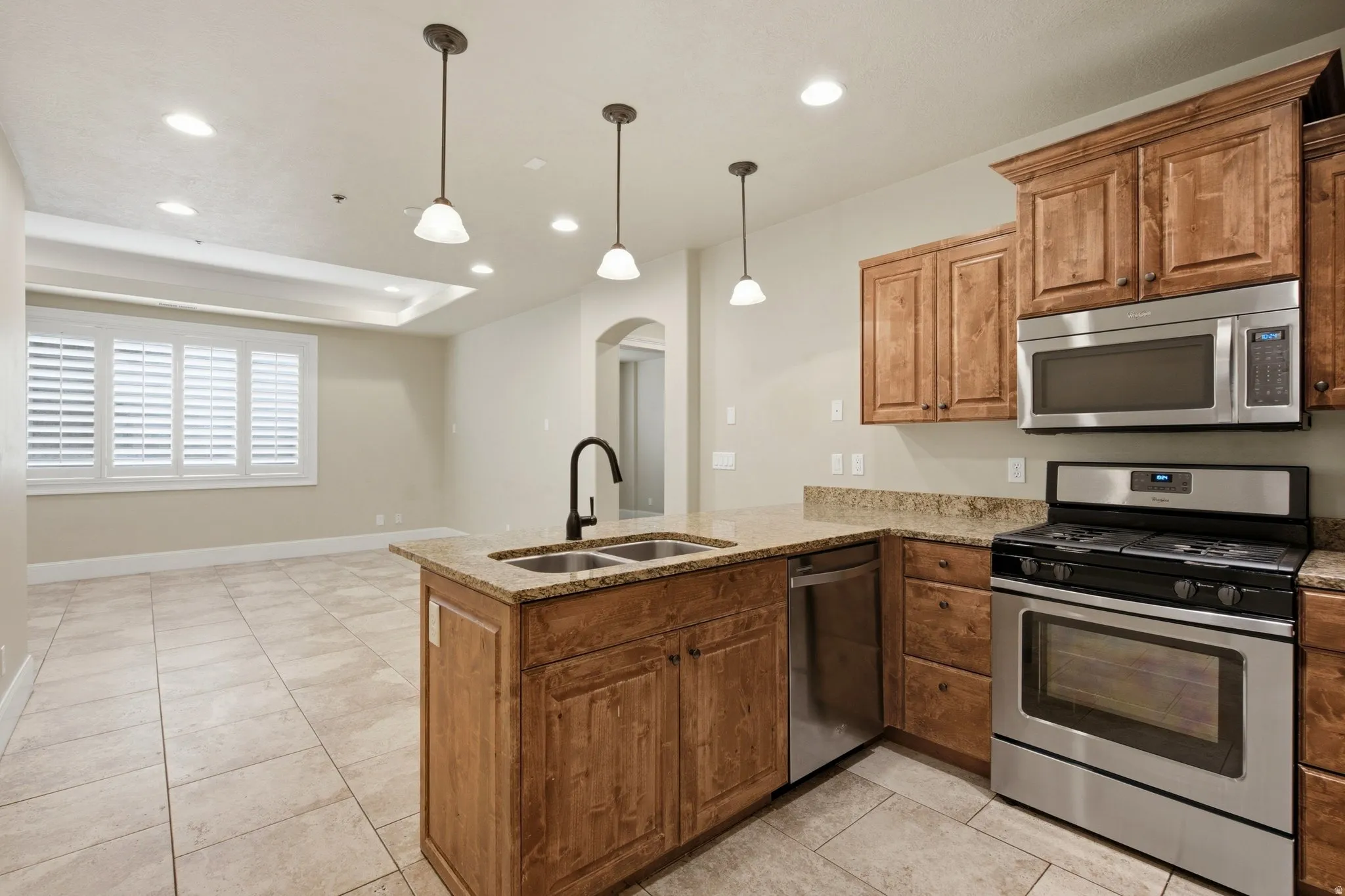 Kitchen featuring recessed lighting, a central island with a double basin sink and gooseneck faucet, light wood cabinetry, stainless steel appliances, and a tile floor