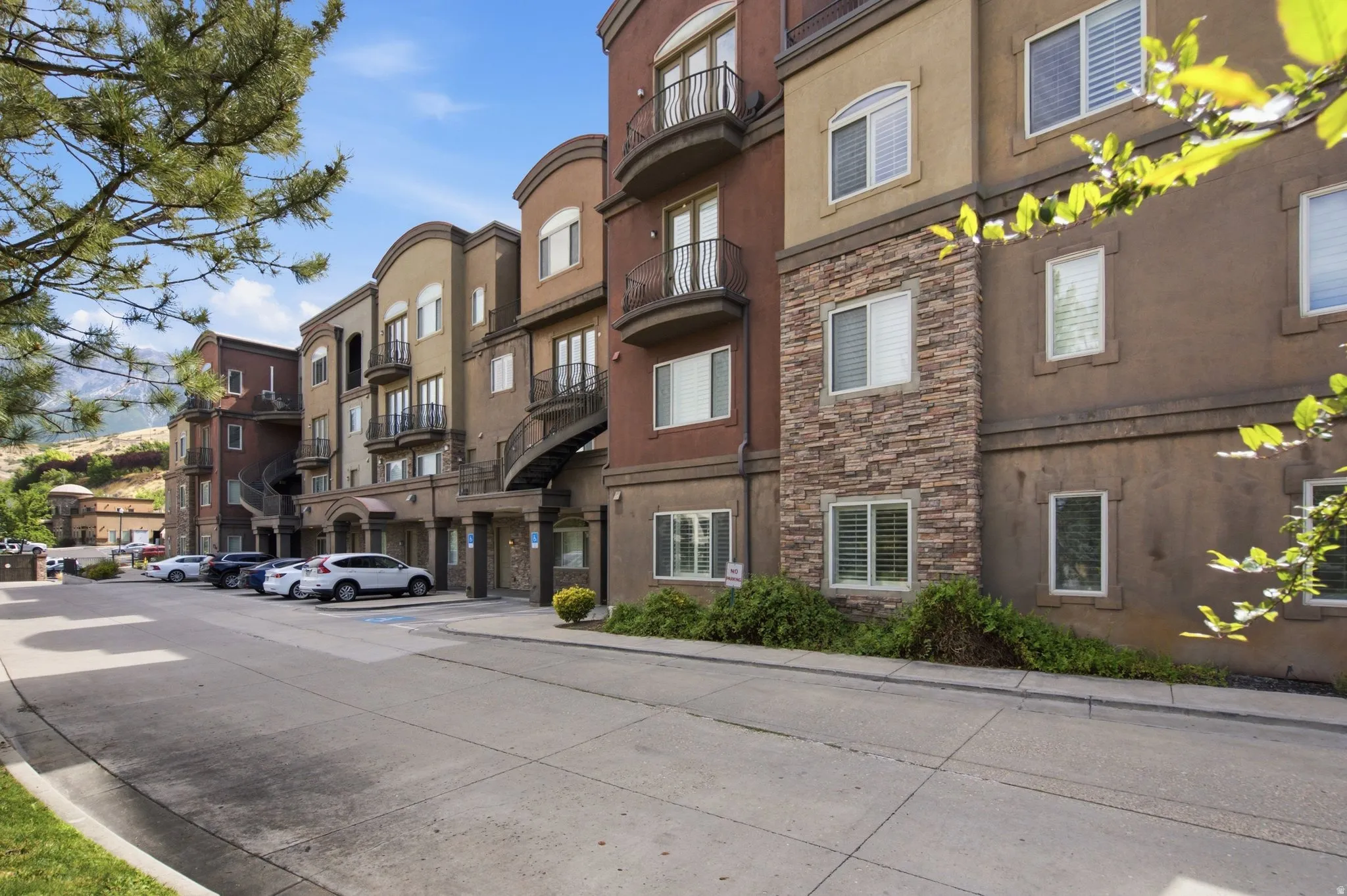Multi-story residential building featuring balconies with wrought iron railings, stone veneer accents, and stucco exterior finishes