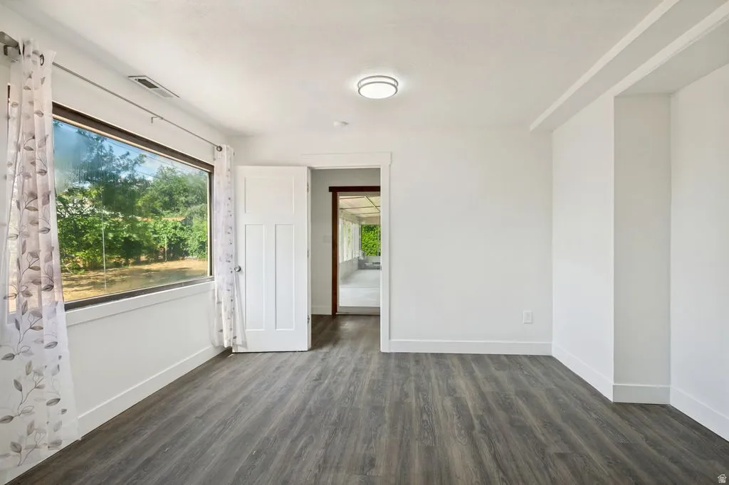 Spacious room featuring wood-finish flooring, a large picture window, recessed ceiling light, and a white paneled door