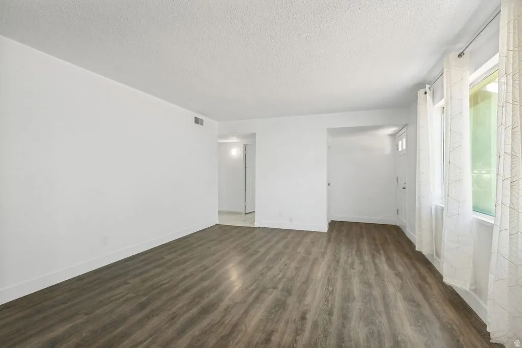 Spacious room featuring wood-finish flooring, white walls, and a recessed air vent