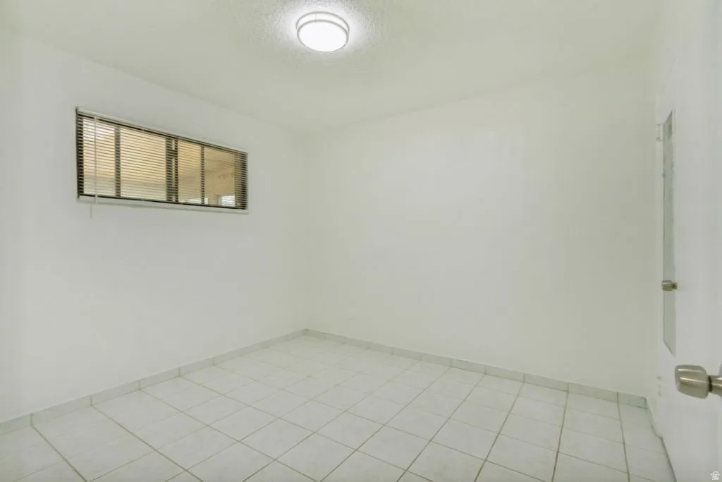 Bright room featuring tiled flooring, a window with horizontal blinds, a flush mount ceiling light fixture, and a solid interior door with a brushed nickel knob