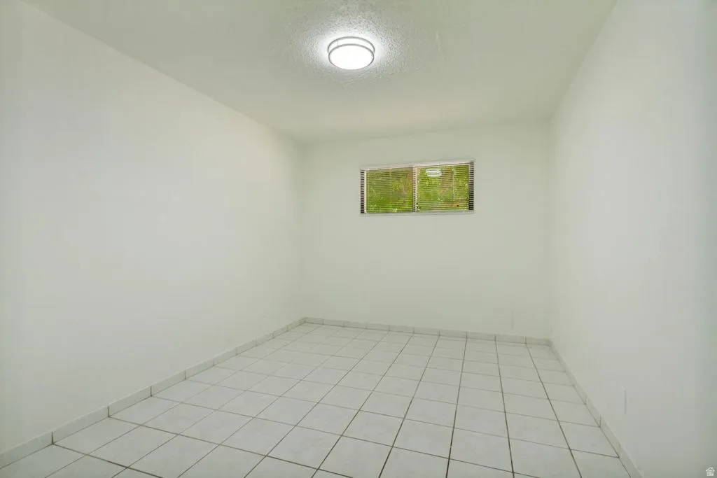 Windowed room with white walls, tiled flooring, and an overhead flush-mount light fixture