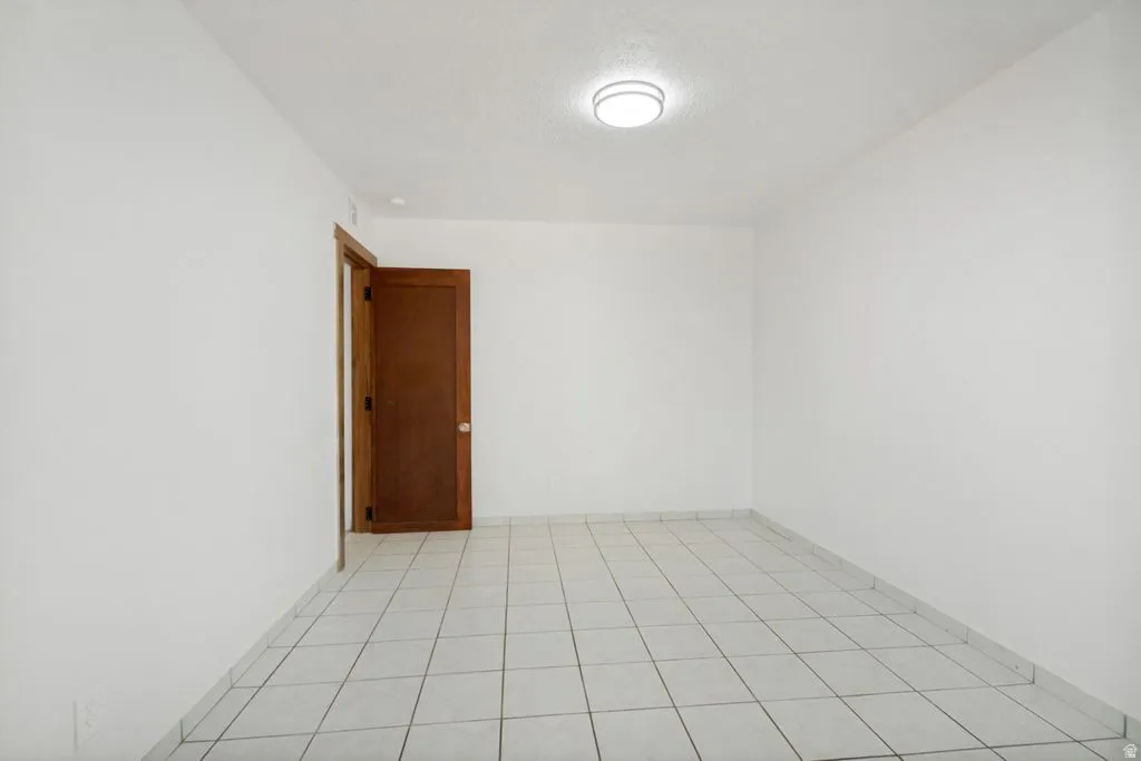 Bright interior space featuring white tile flooring, a solid wood door, and a flush-mount ceiling light fixture