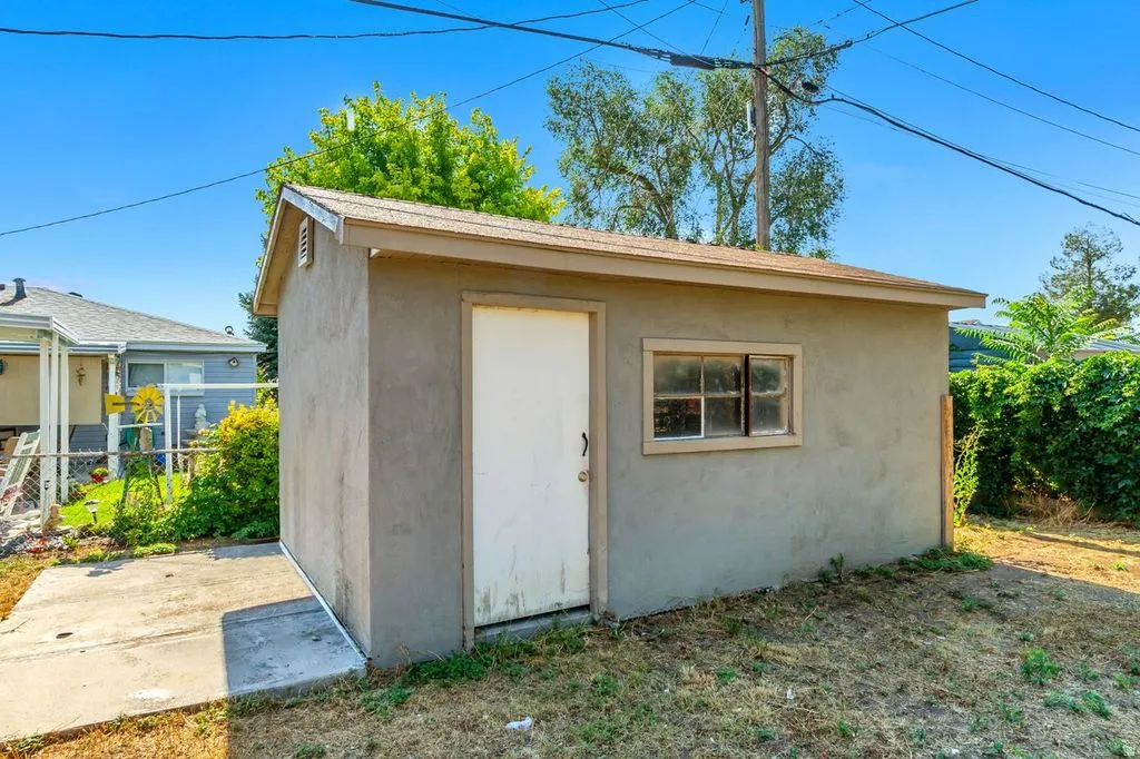 Stucco-finished outbuilding featuring a pitched roof, single window, side door, and adjacent concrete pad