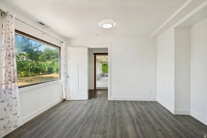 Spacious room featuring wood-finish flooring, a large picture window, recessed ceiling light, and a white paneled door
