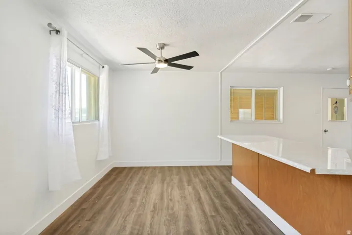 Open-concept living area featuring wood-finish flooring, a contemporary ceiling fan, and a kitchen island with a light-toned countertop
