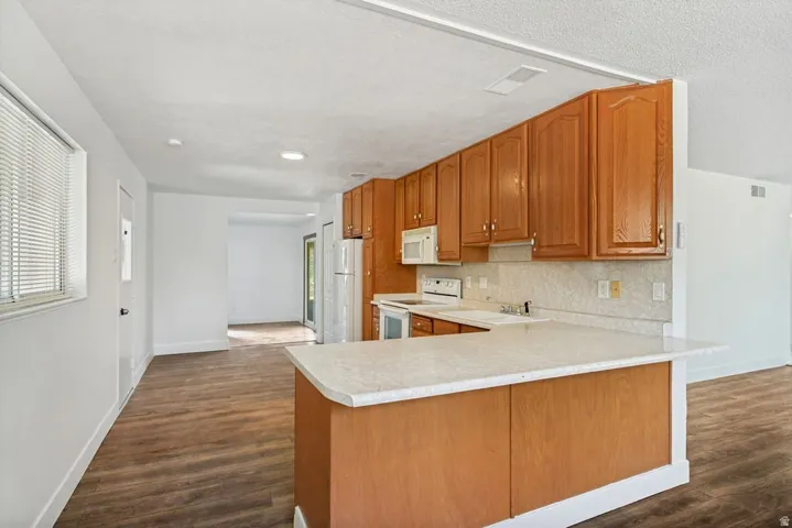 Kitchen featuring wood cabinetry, light-toned countertops, a built-in microwave, and white appliances