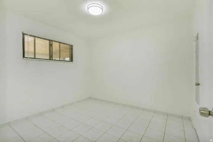Bright room featuring tiled flooring, a window with horizontal blinds, a flush mount ceiling light fixture, and a solid interior door with a brushed nickel knob