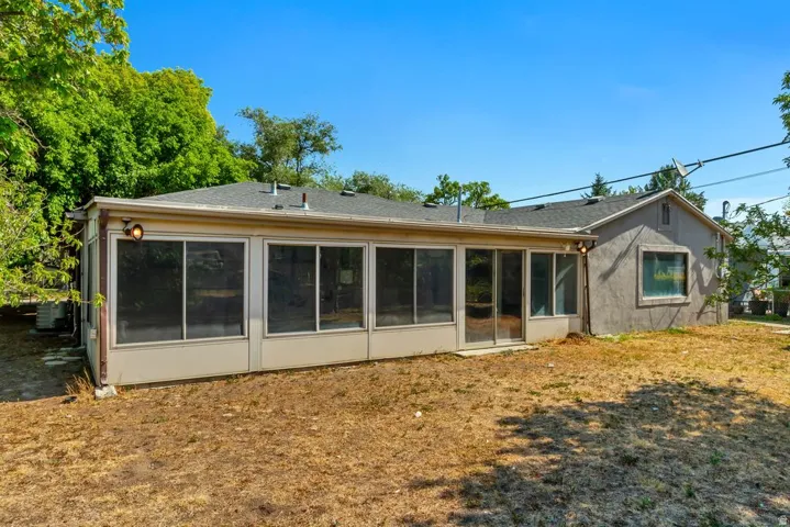 Rear facade featuring an enclosed patio, sliding glass door, shingle roofing, and stucco exterior