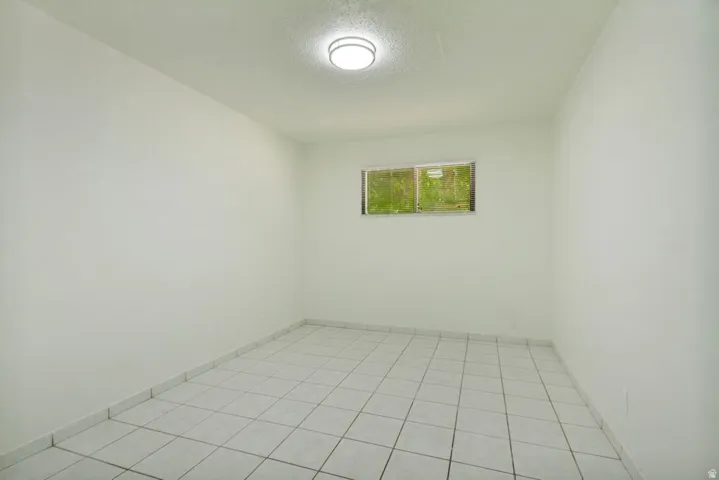 Windowed room with white walls, tiled flooring, and an overhead flush-mount light fixture