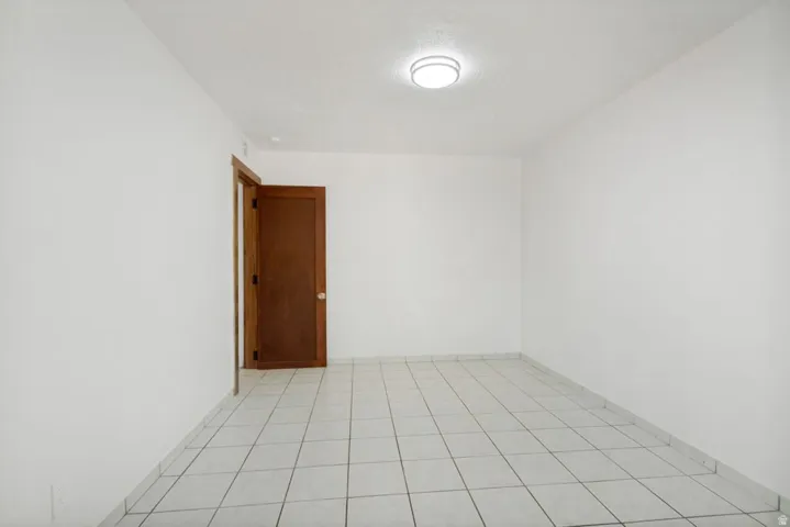 Bright interior space featuring white tile flooring, a solid wood door, and a flush-mount ceiling light fixture