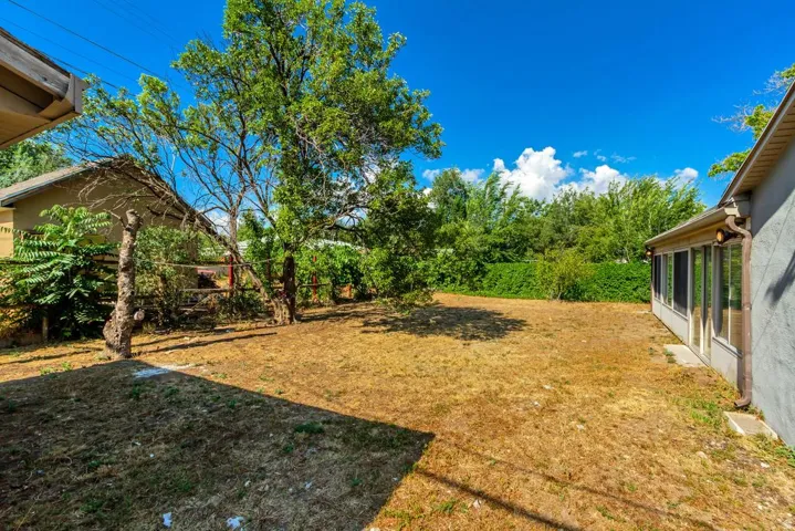 Expansive backyard featuring a partially enclosed patio, mature trees, and a wooden fence along the property line