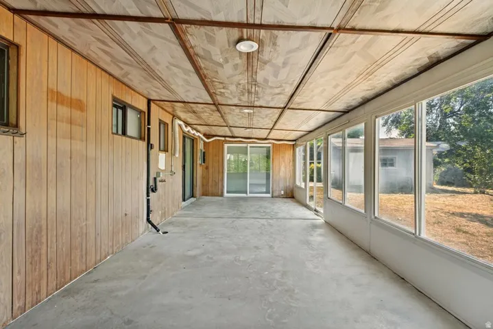 Enclosed patio featuring a concrete floor, wood-paneled wall, and a full wall of windows