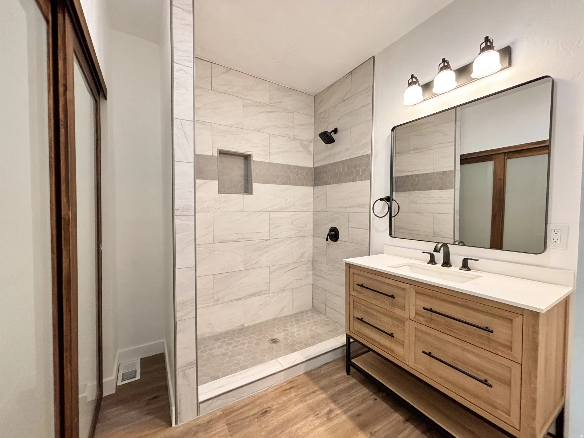 Walk-in shower with tiled walls and a hex tile floor, featuring a built-in niche