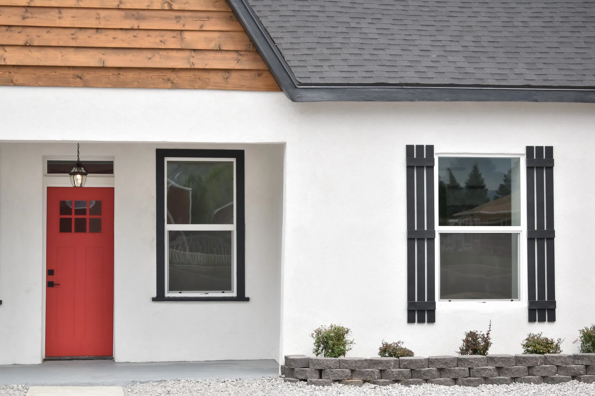 White stucco exterior with a bright red entry door featuring glass panes and a hanging porch light