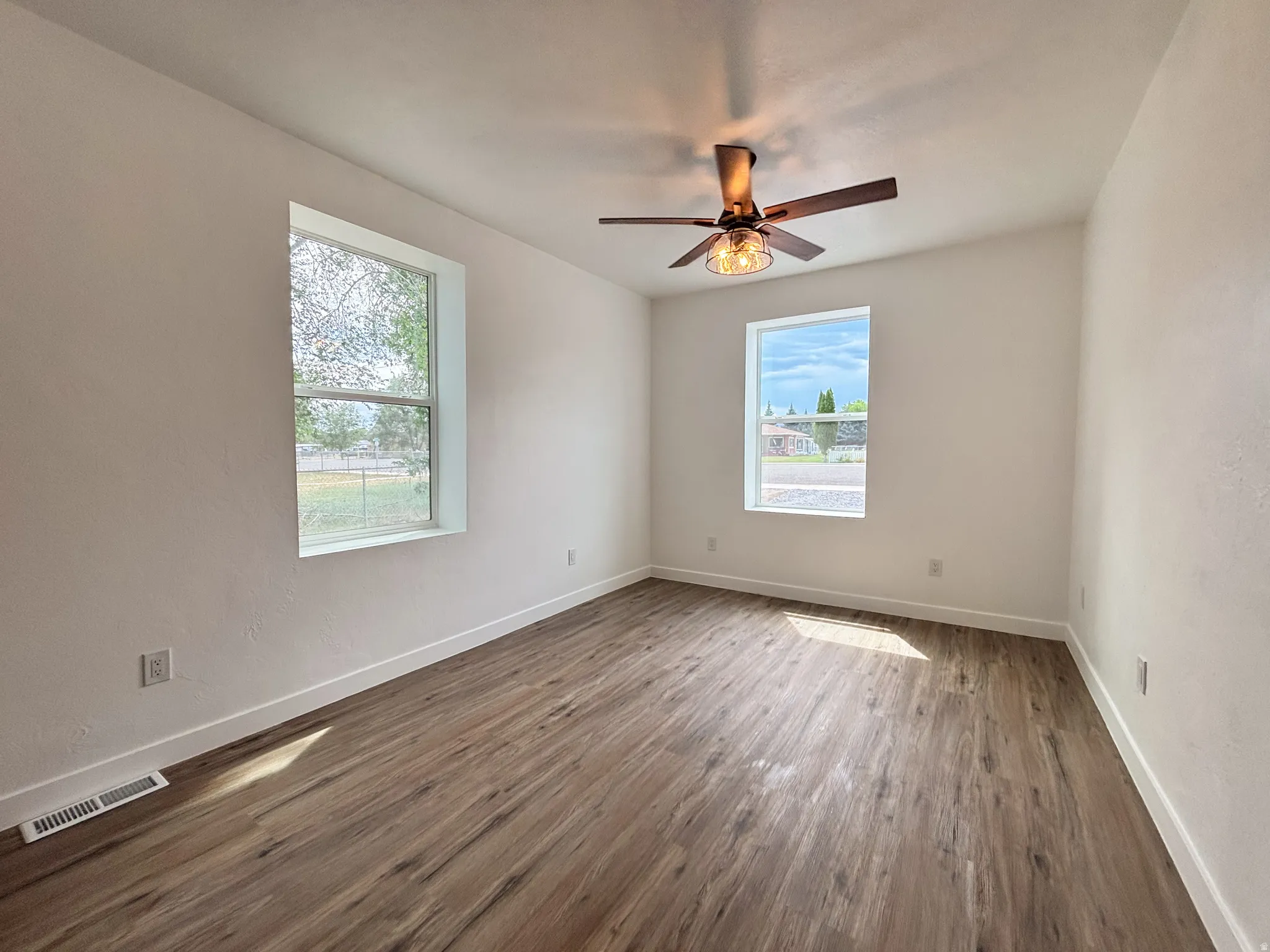 Room with wood-finish flooring, white walls, and a ceiling fan with integrated lighting