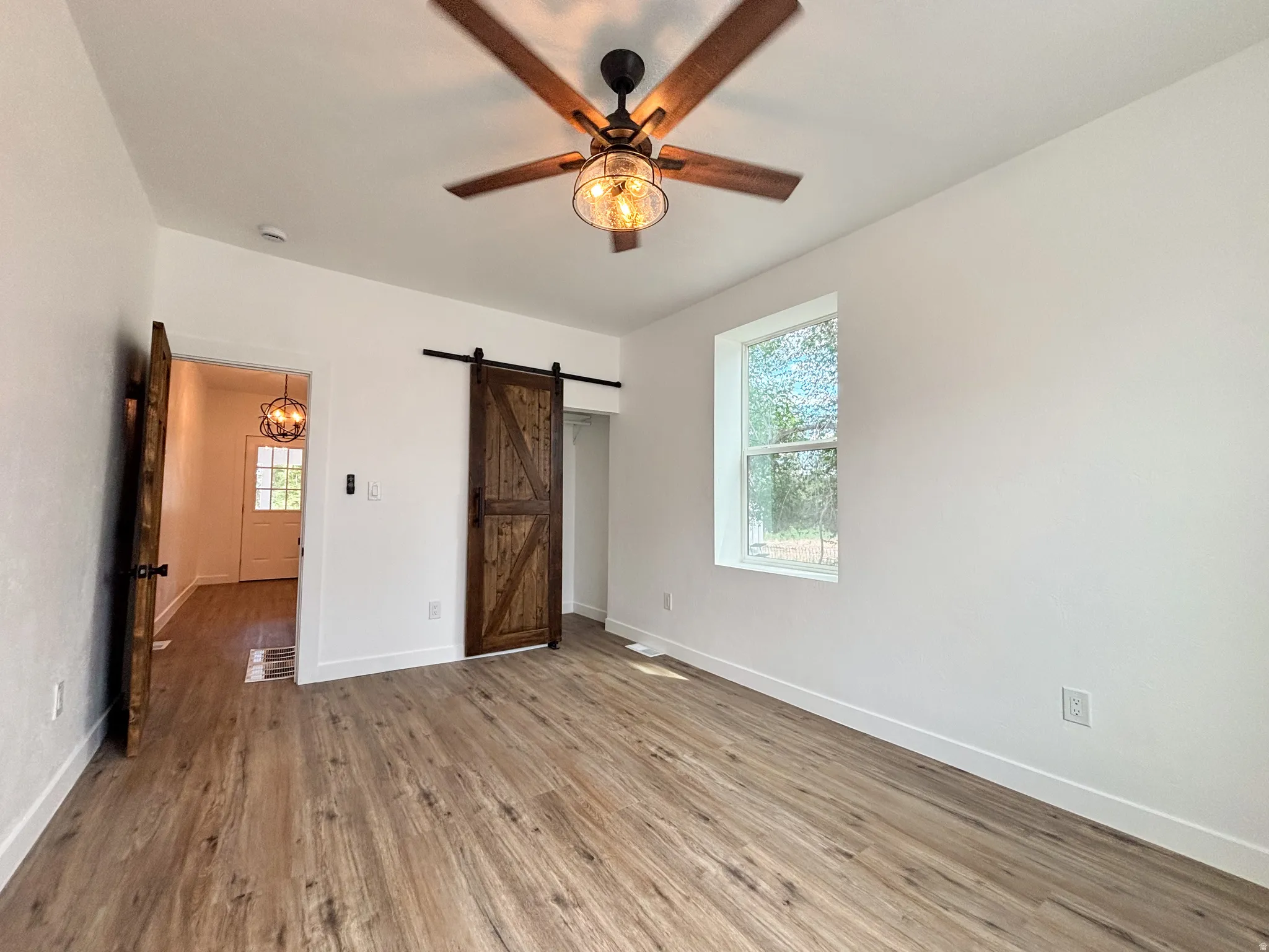 Spacious interior room featuring wood-finish flooring, a ceiling fan with light fixture, and a single window