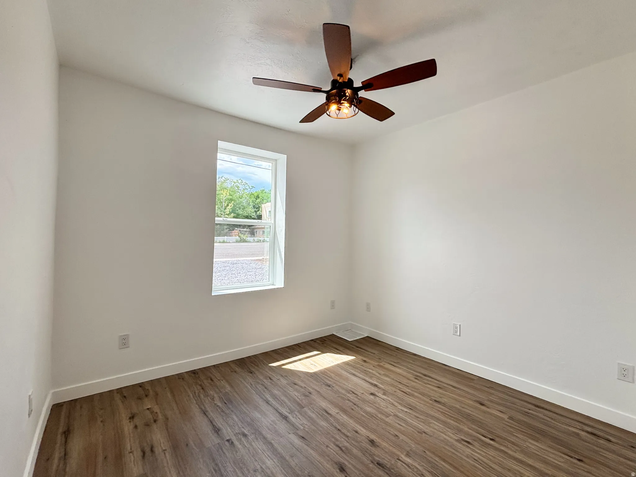 Bright interior space featuring wood-finish flooring, white baseboards, and a contemporary ceiling fan with integrated lighting