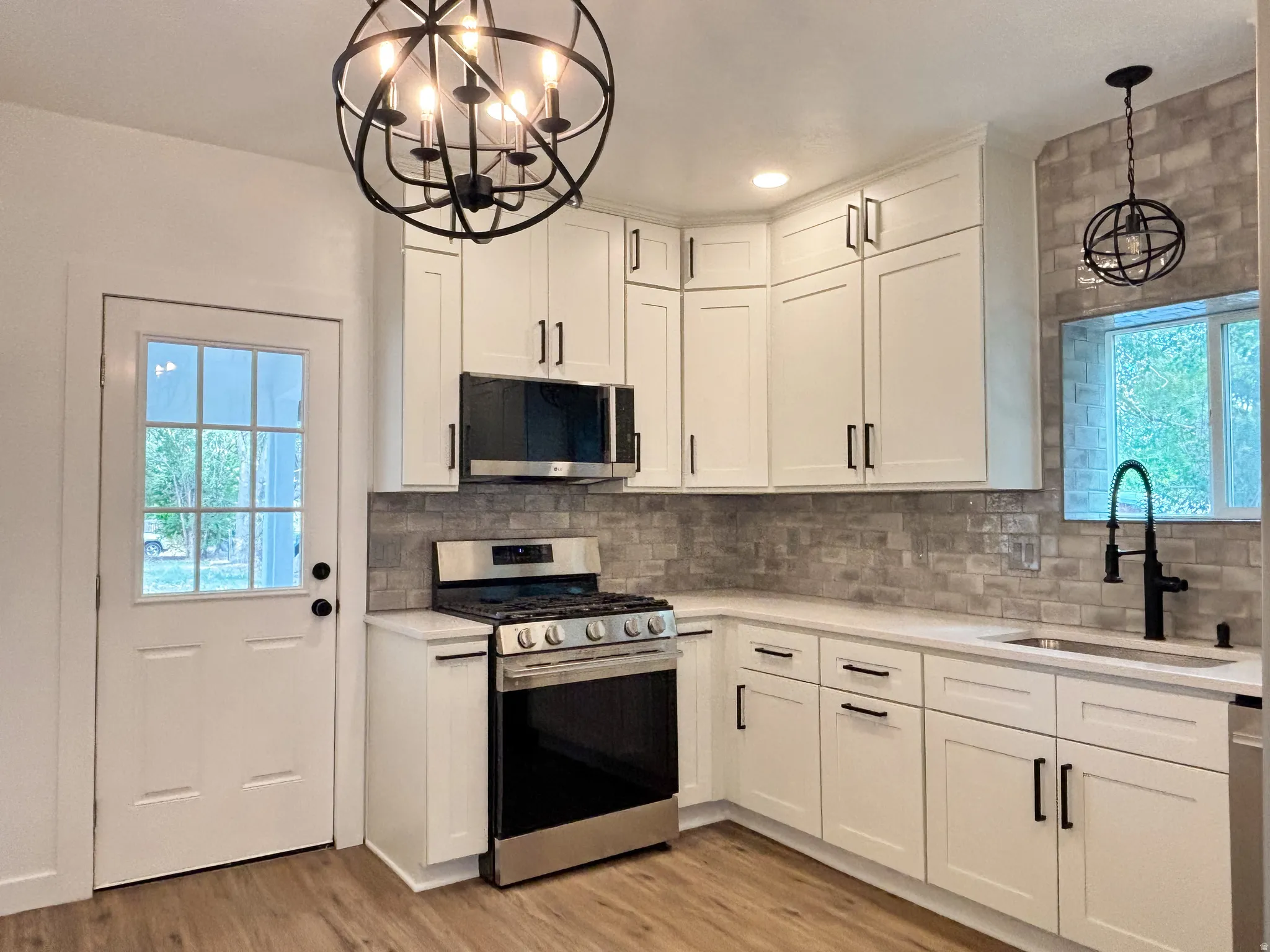 Kitchen featuring white shaker cabinetry, stainless steel appliances, a grey subway tile backsplash, and wood-finish flooring