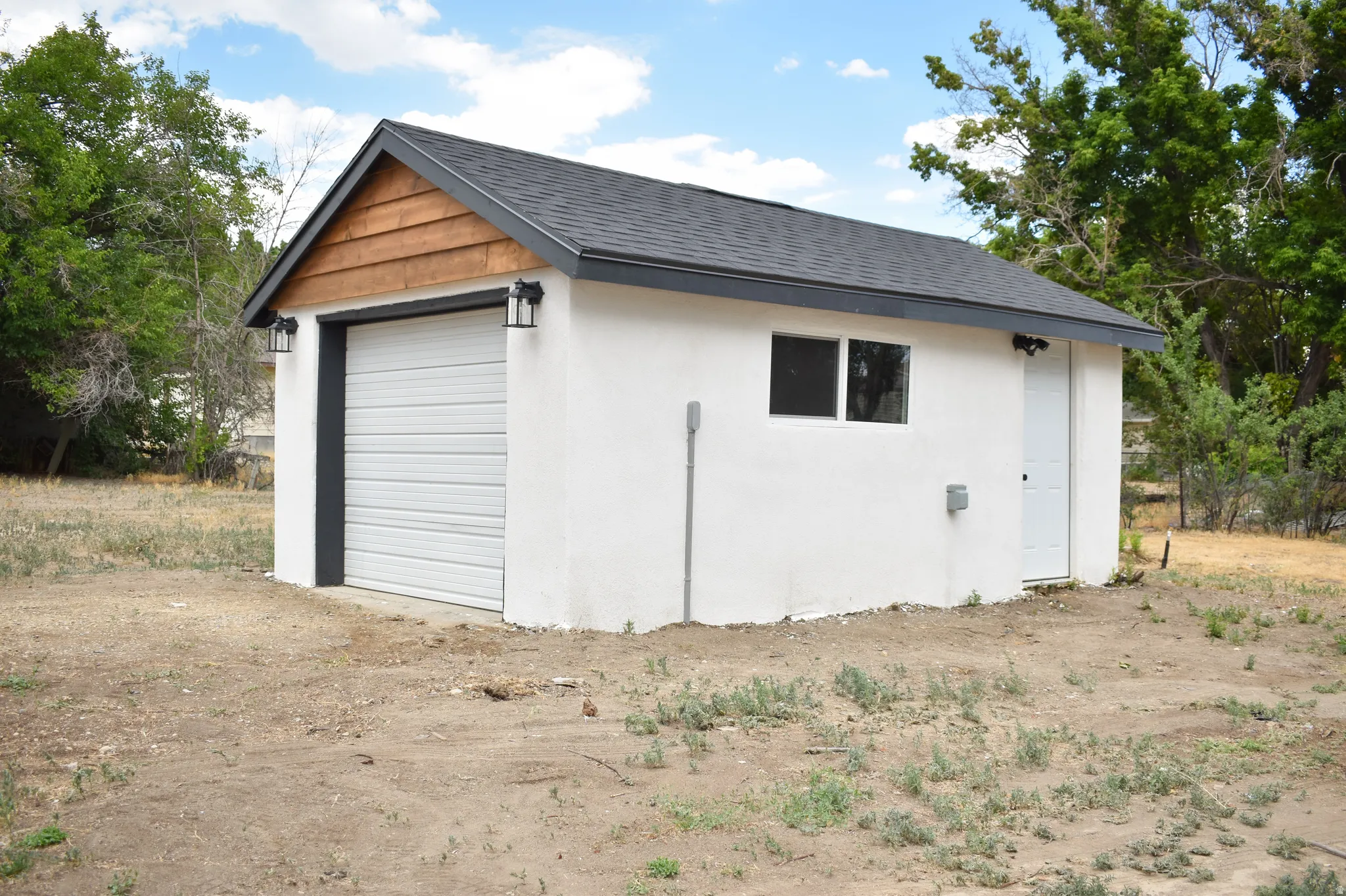 Detached structure featuring a white stucco exterior, dark shingle roof, and a wood-paneled gable